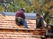 workers placing wooden shingles on top of cabin