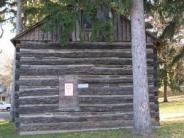 old log cabin, side view with window, shadow of a tree branch on its side, pine dree draping over it